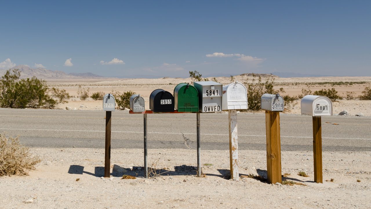 A row of numbered curbside mailboxes along a sunlit road